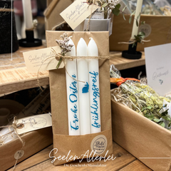 Stabkerzen mit einer türkisfarbenen Schrift beschriftet stehen schön dekoriert auf einem Holztisch