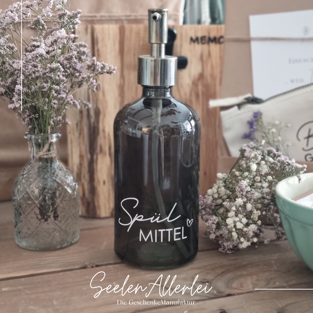 grüner Seifenspender mit der Aufschrift Spülmittel steht auf einem holzuntergrund mit Trockenblumen dekoriert