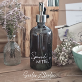 grüner Seifenspender mit der Aufschrift Spülmittel steht auf einem holzuntergrund mit Trockenblumen dekoriert