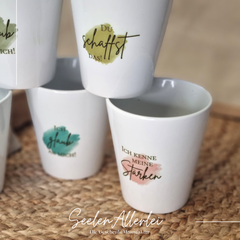 Porzellanbecher mit Affirmationen wie "Du schaffst das", "Ich glaub an Dich", "Ich kenne meine Stärken" etc. auf verschieden farbigen Hintergründen.