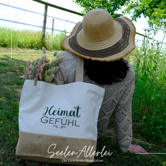 Shoppertasche wird von einer Frau, die man von hinten sieht über der Schulter getragen. Sie enthält einen Strauß Trockenblumen
