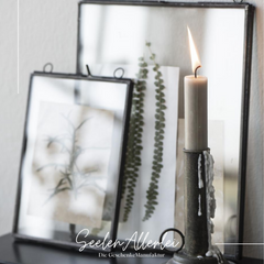 Glasrahmen schwarz mit Kerze im Vordergrund lehnen an der Wand