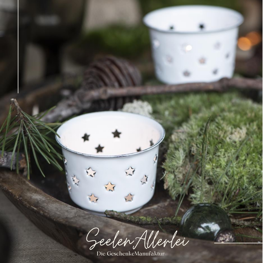 Teelichthalter aus Emaille in weiß mit zahlreichen sternfömigen Löchern steht auf eiem Holztablett mit Dekoration