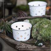 Teelichthalter aus Emaille in weiß mit zahlreichen sternfömigen Löchern steht auf eiem Holztablett mit Dekoration