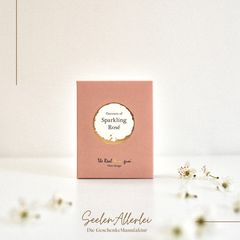 Wine Gums in der Geschmacksrichtung sparkling rose in rosefarbener Verpackung auf einem Weißen tisch mit weißem HIntergrund Kirschblüten als Deko.