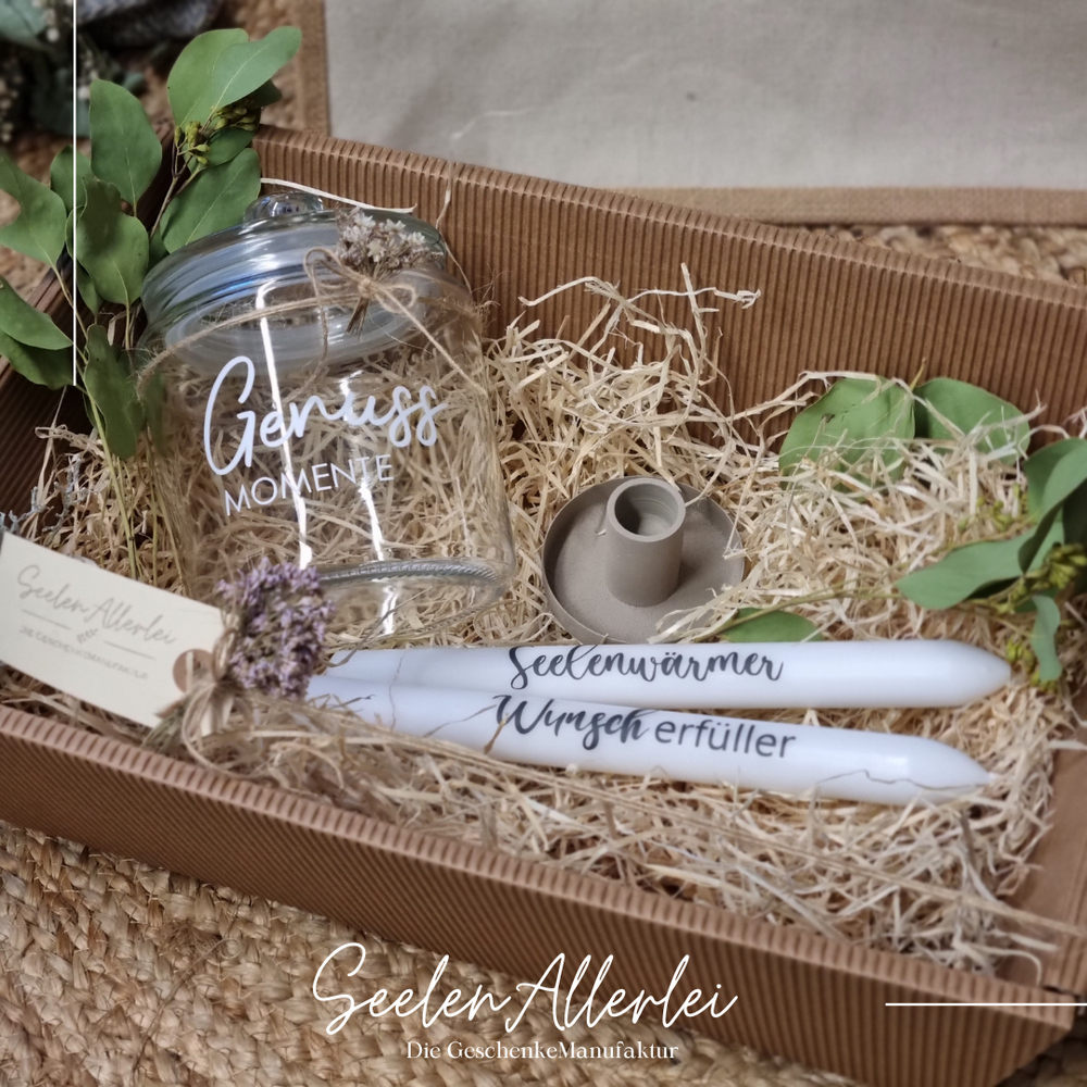 Bonbonglas in einem Geschenkkorb zusammen mit zwei beschrifteten Stabkerzen und einem Kerzenhalter