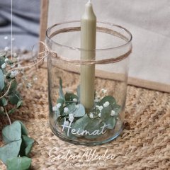 Individuelles Windlicht mit Gravur Heimat, dekoriert mit Eukalyptus und weißer Stabkerze im natürlichen Setting