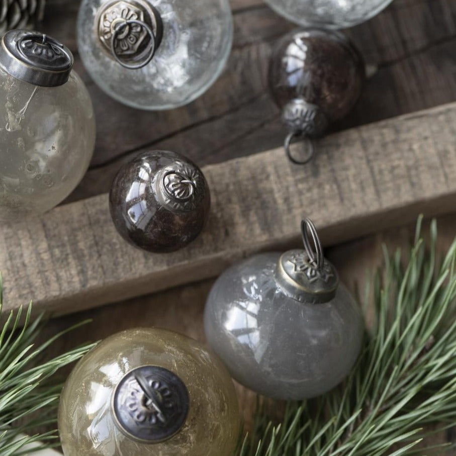 Baumkugeln aus Glas in verschiedene Farben und Größen liegen auf einem Holztisch mit Tannenzweigen als Dekoration