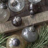 Baumkugeln aus Glas in verschiedene Farben und Größen liegen auf einem Holztisch mit Tannenzweigen als Dekoration