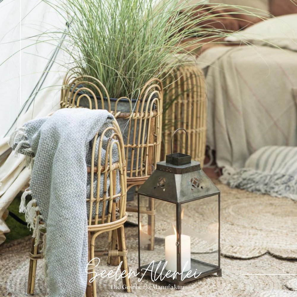 Bambuskörbe entweder mit Pflanzen gefüllt oder mit Kuscheldecke - davor steht eine Laterne mit brennender Kerze