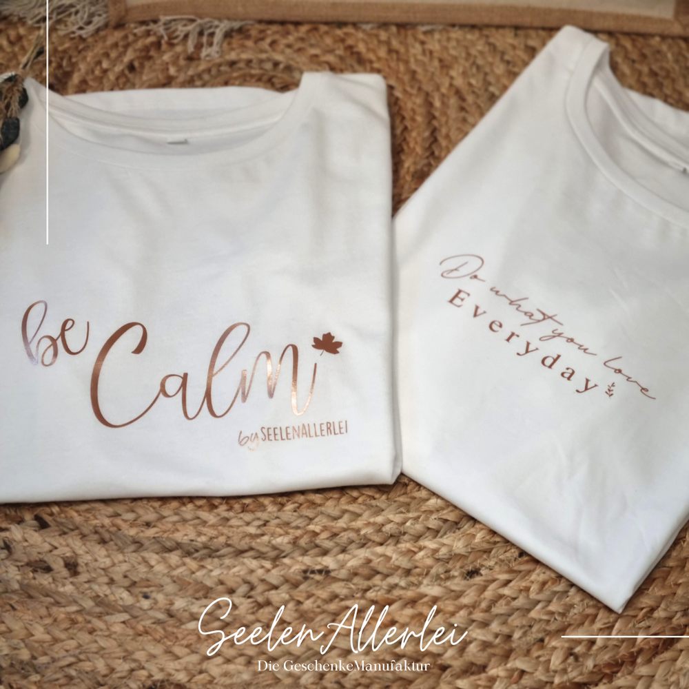 zwei weiße Shirts mit unterschiedlichen Sprüchen aufgedruckt liegen auf einem schönen Teppich zur auswahl