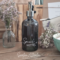 grüner Seifenspender mit der Aufschrift Spülmittel steht auf einem holzuntergrund mit Trockenblumen dekoriert