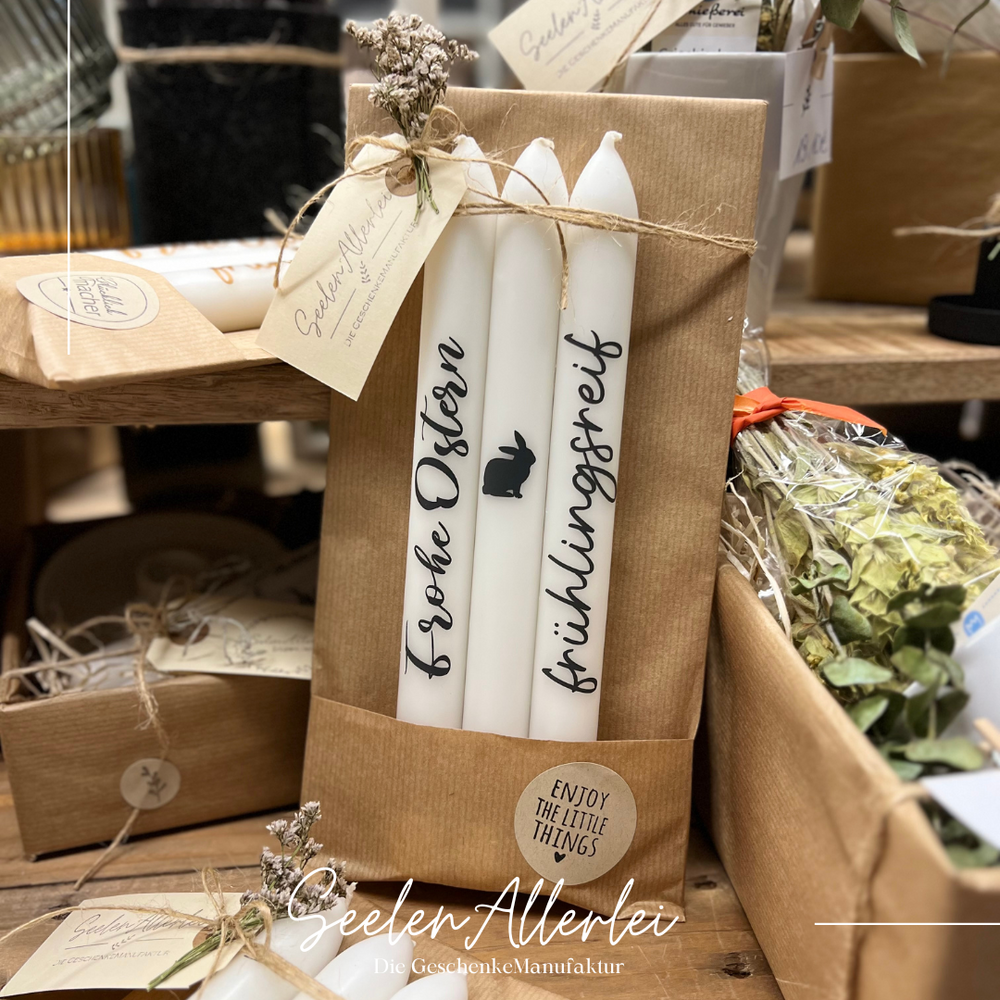 Stabkerzen mit anthrazitfarbener Schrift frühlingsrerif und Frohe Ostern stehen auf einem Holztisch