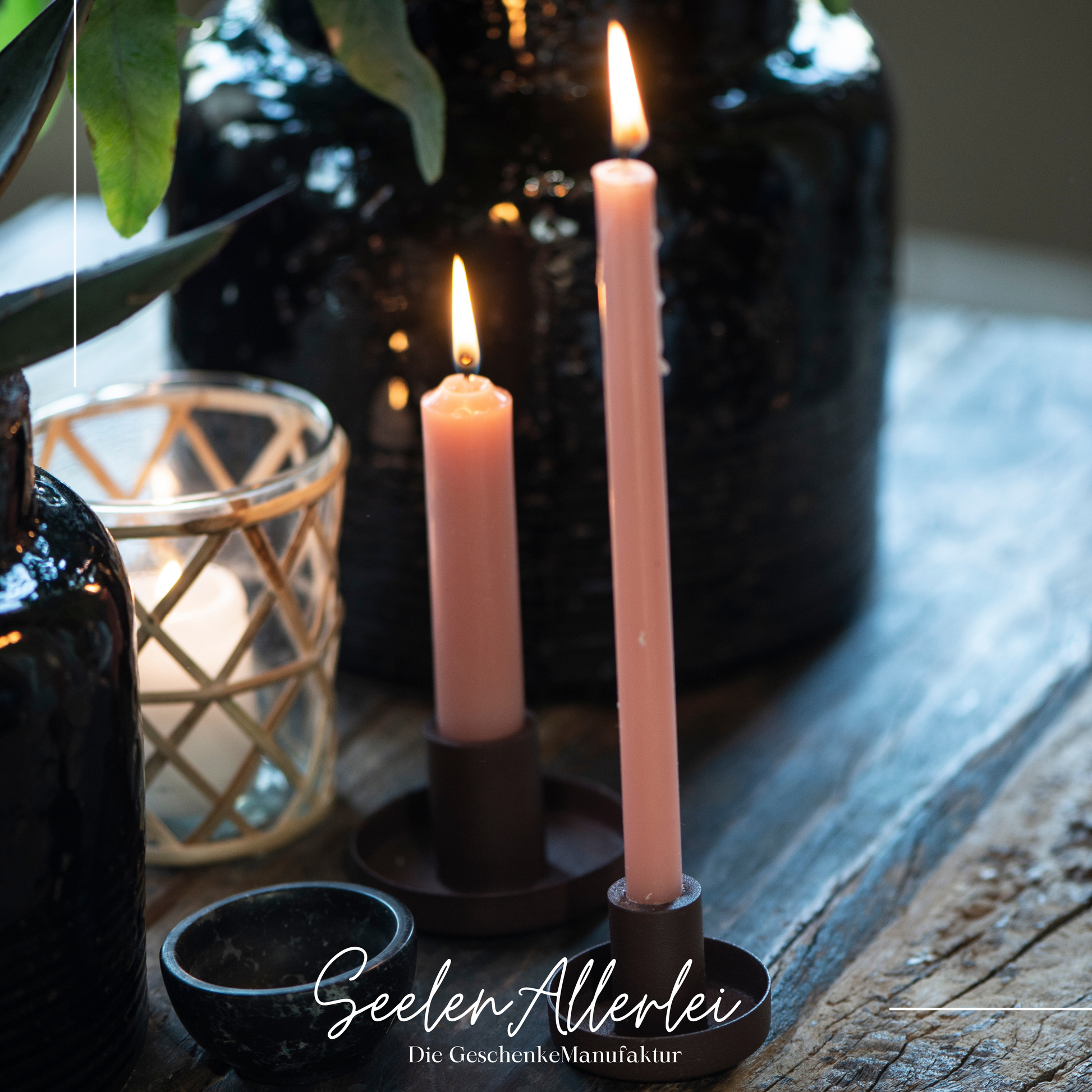 Kerzenhalter in schwarz für dünne Kerze steht mit einer brennenden dünnen Kerze neben einem Kerzenhalter für normale Stabkerzen.