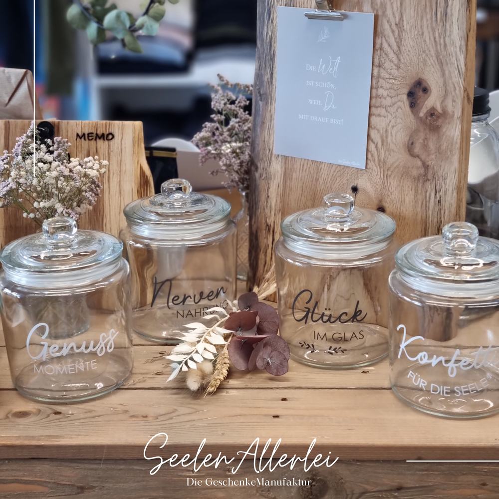 4 verschiedene Vorratsgläser mit unterschiedlicher Aufschrift auf einem Holztisch vor Memobrettern