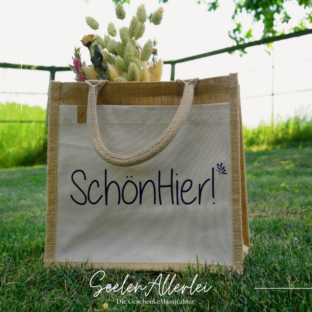 Markttasche mit der Aufschrift Schön hier auf einer wiese im hintergrund ein Feld und ein Zaun