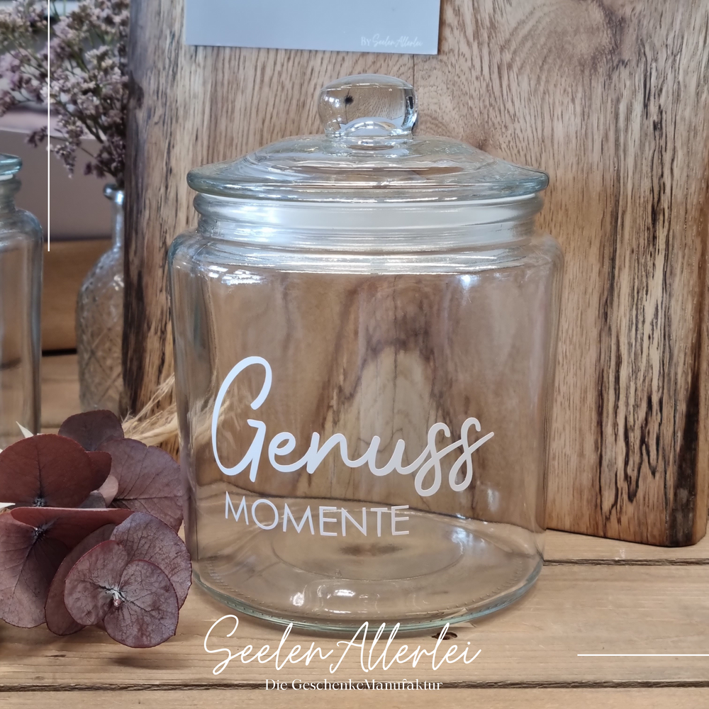 Genussmoment steht in weiß auf einem Genussmoment mit Glasdeckel vor einem Holzmemoboard