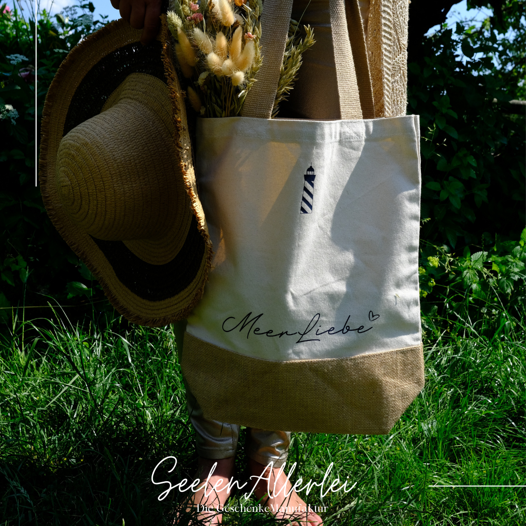 Aufnahme einer Tasche, die von einer Frau getragen wird mit der Aufschrift Meerliebe, die Frau steht mit nackten Füßen im Gras und hält zur Tasche inen Sonnenhut in Händen