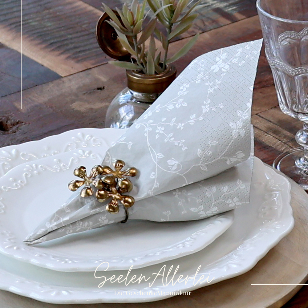 Serviette grau von Chic antique mit einem messingfarbenen Serviettenhalter auf einem gedeckten Teller