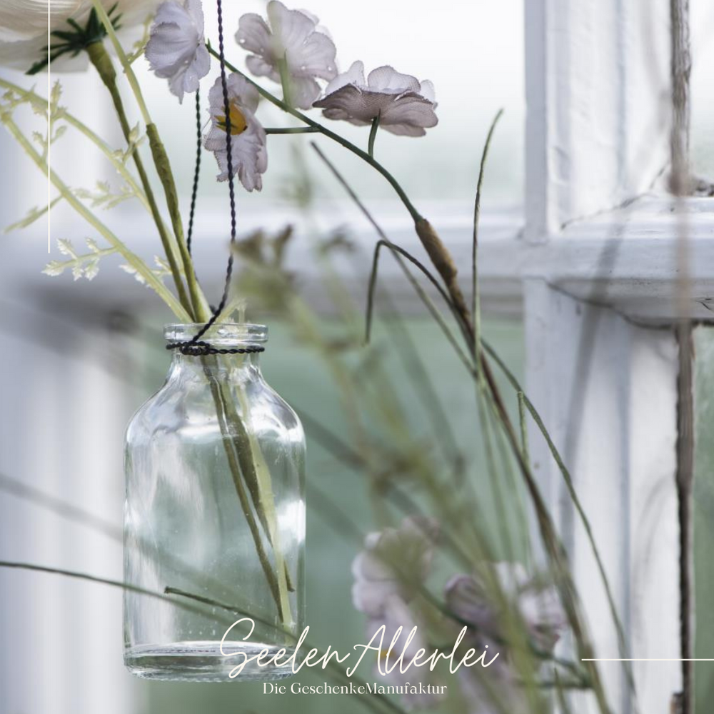 kleine Glasflasche häng vor ein paar Blumen an einem Zweig