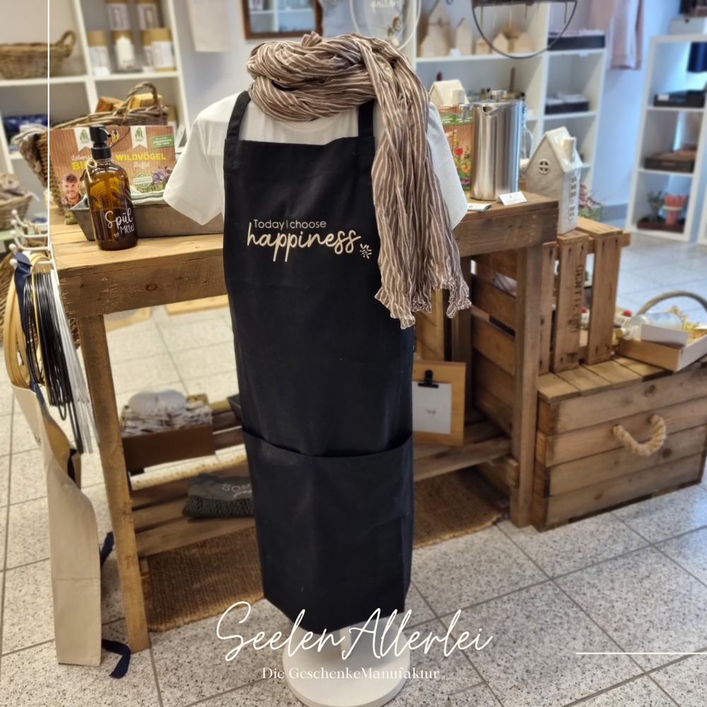 Kochschürze auf einer Kleiderpuppe in der GeschenkeManufaktur Seelenallerlei vor einem Präsentationstisch aus Holz mit verschiedenen Geschenkkörben