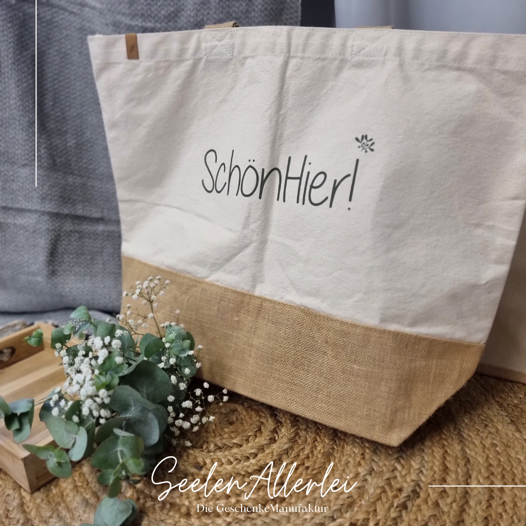 große Shoppertasche mit dem Spruch Schön hier! steht auf einem Teppich mit Dekoration