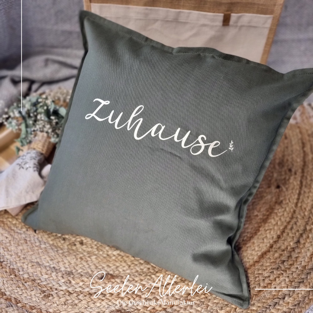 Kissen in grau mit dem Aufdruck Zuhause liegt auf einem Teppich