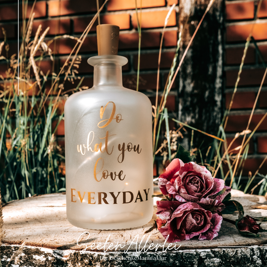 Apothekerflasche satiniert mit Spruch steht im Garten auf einer Holzscheibe mit Rosendekoration