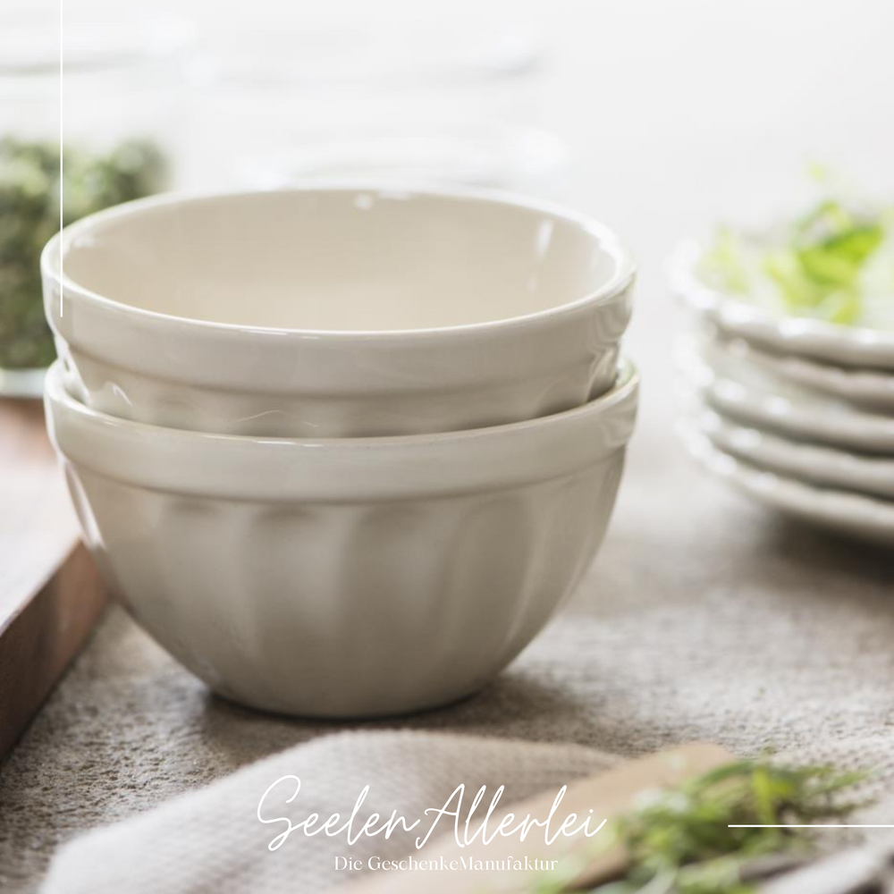 zwei Müslischalen in der Farbe buttercream stehen ineinandergestapelt auf einem Tuch mit Tellern und Servietten