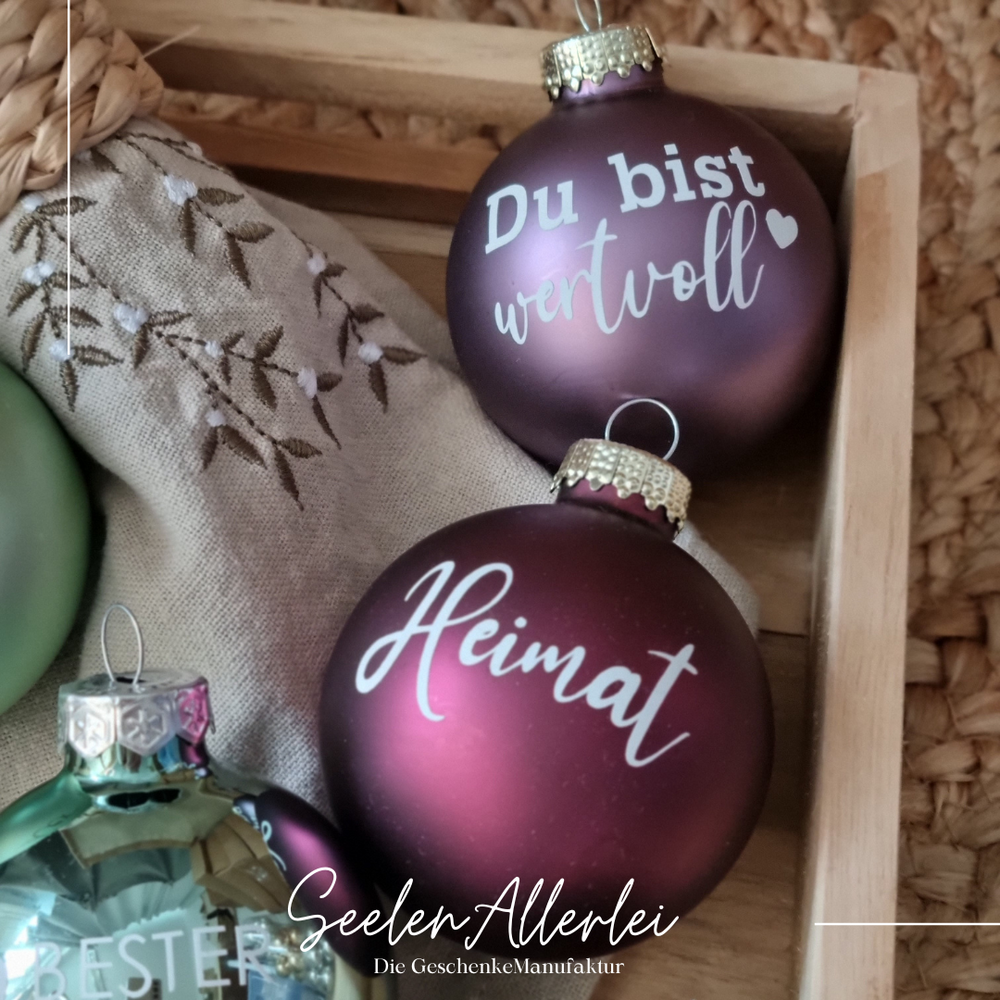 rote kugel mit der aufschrift heimat und altosa sanierte Kugel mit der Aufschrift Du bist wertvoll in einem Tablett