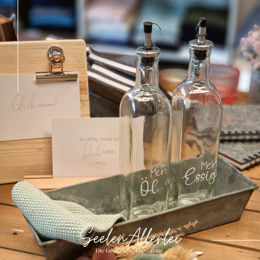essig und öl Flaschen stehen zusammen mit einem spültuch in einer Metallschale vor einem Memeoboard aus Holz auf einem Holztisch