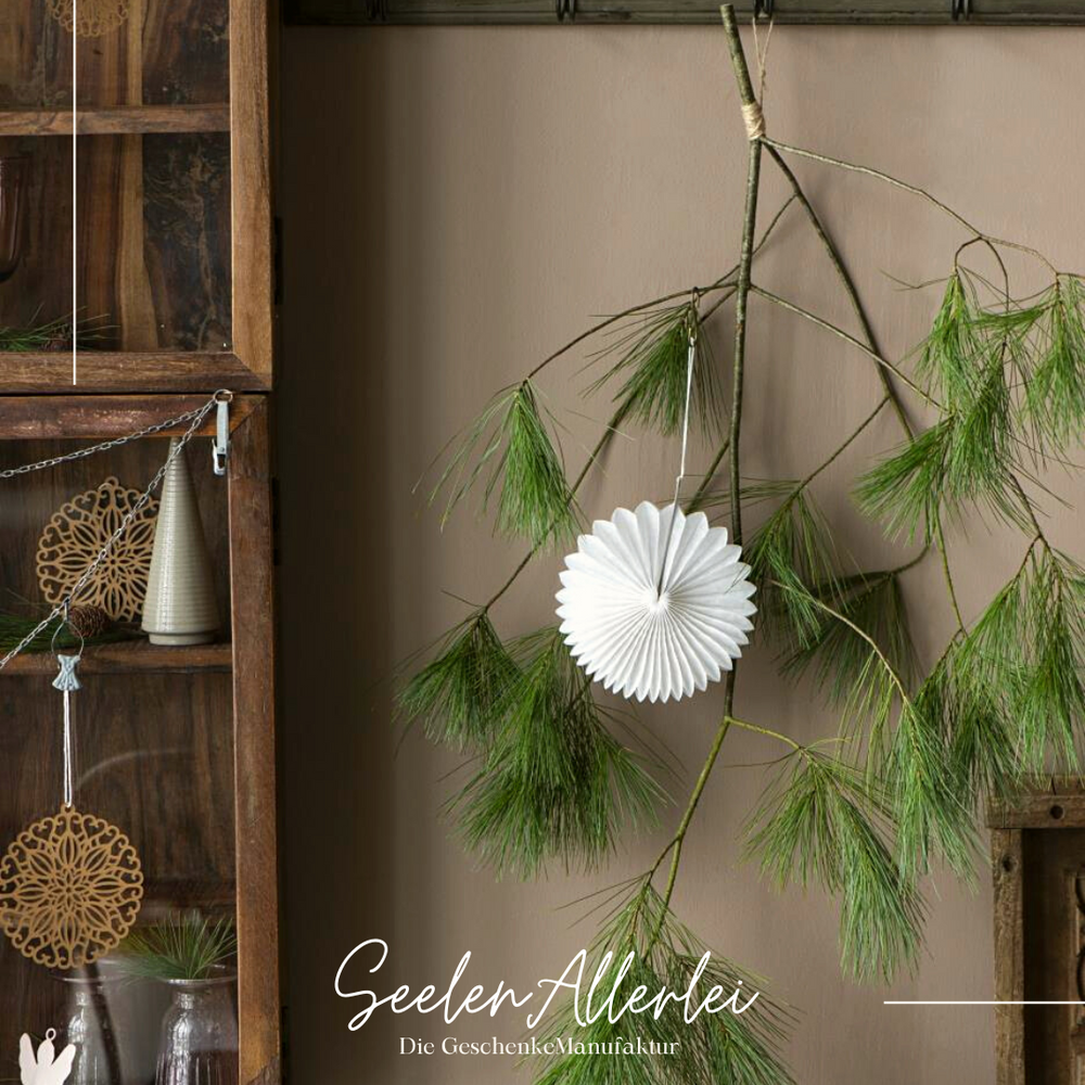 weißes Papierornament in rund hängt an einem Zweig an der Wand neben einem Holzschrank
