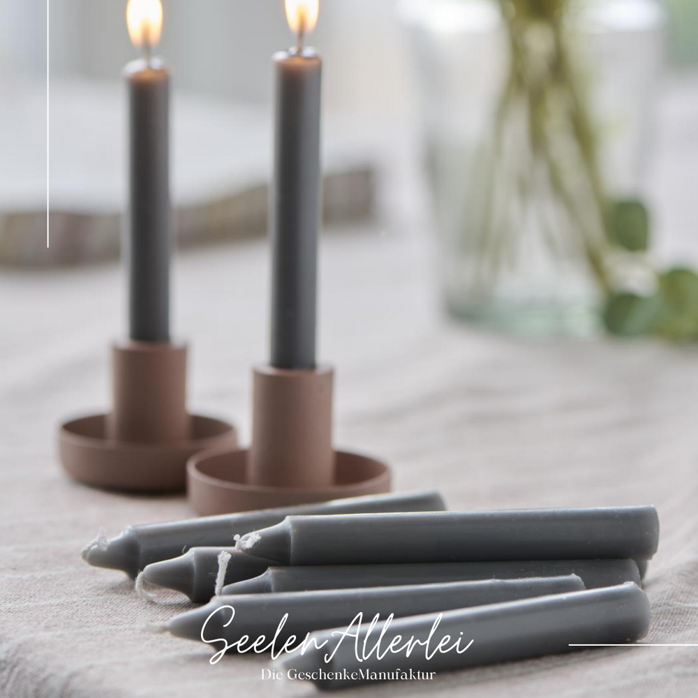 Kerzenständer aus metall in der Farbe malva mit brennenden Kerzen auf einem Tisch, davor liegen blaue Kerzen auf der tischdecke