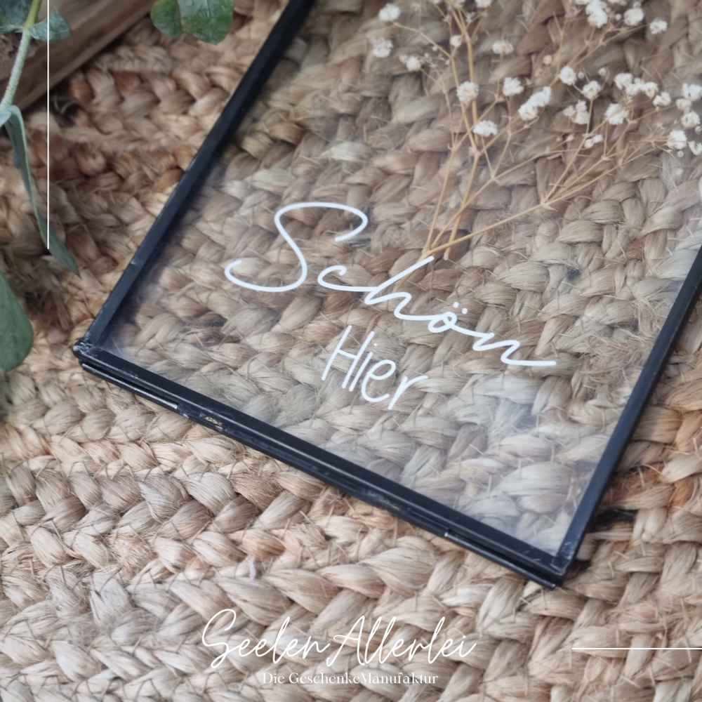 schwarzer kleiner Glasrahmen mit der Aufschrift Schön hier in weißer Schrift mit trockenblumen dekoriert