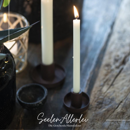 der schwarze Kerzenhalter für dünne kerzen steht mit einer brennenden Kerze direkt neben dem Kerzenhalter für normale Stabkerzen.