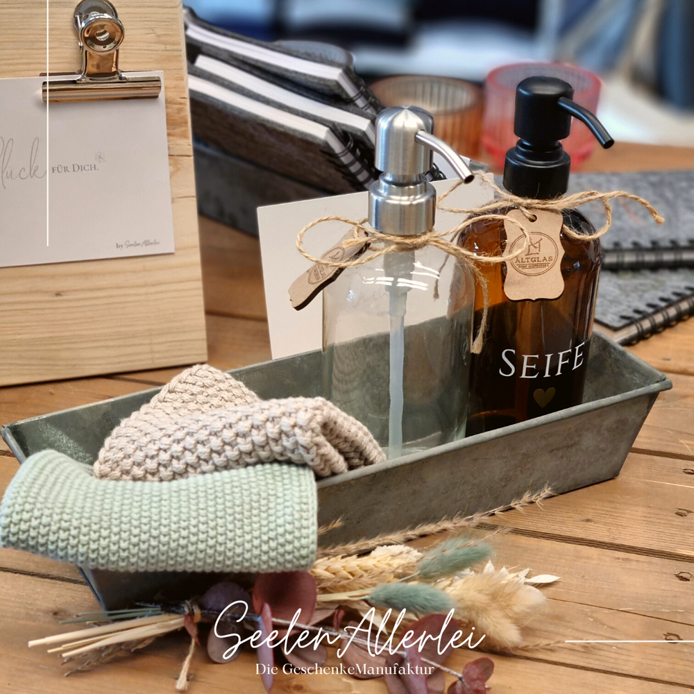 Topflappen und Spüllappen mit zwei Seifenspendern aus Glas in einer Metallschale auf einem Holztisch