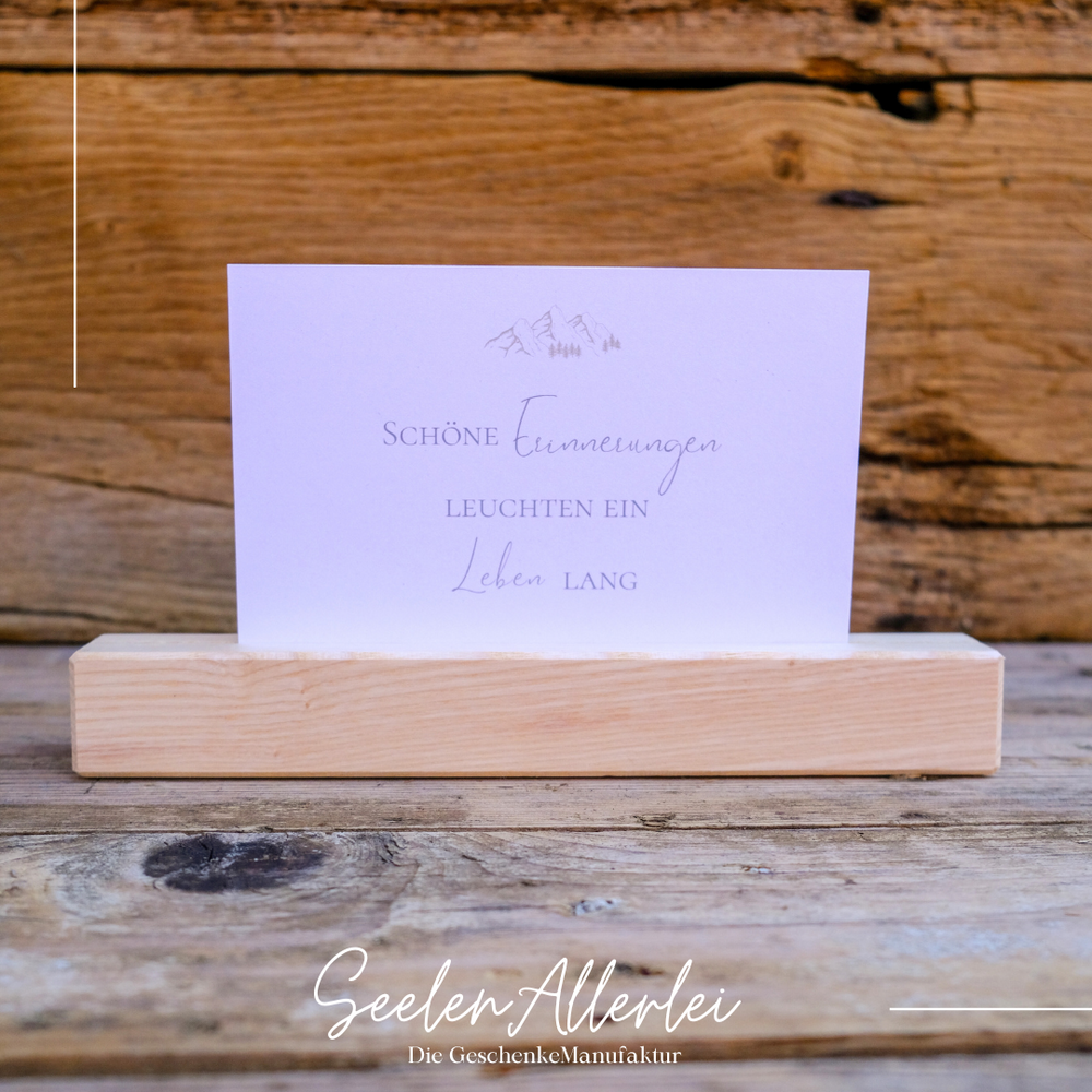 Schöne Erinnerungen leuchten ein Leben lang steht auf einer Karte, die in einem Kartenhalter steht. beides vor einer Holzwand
