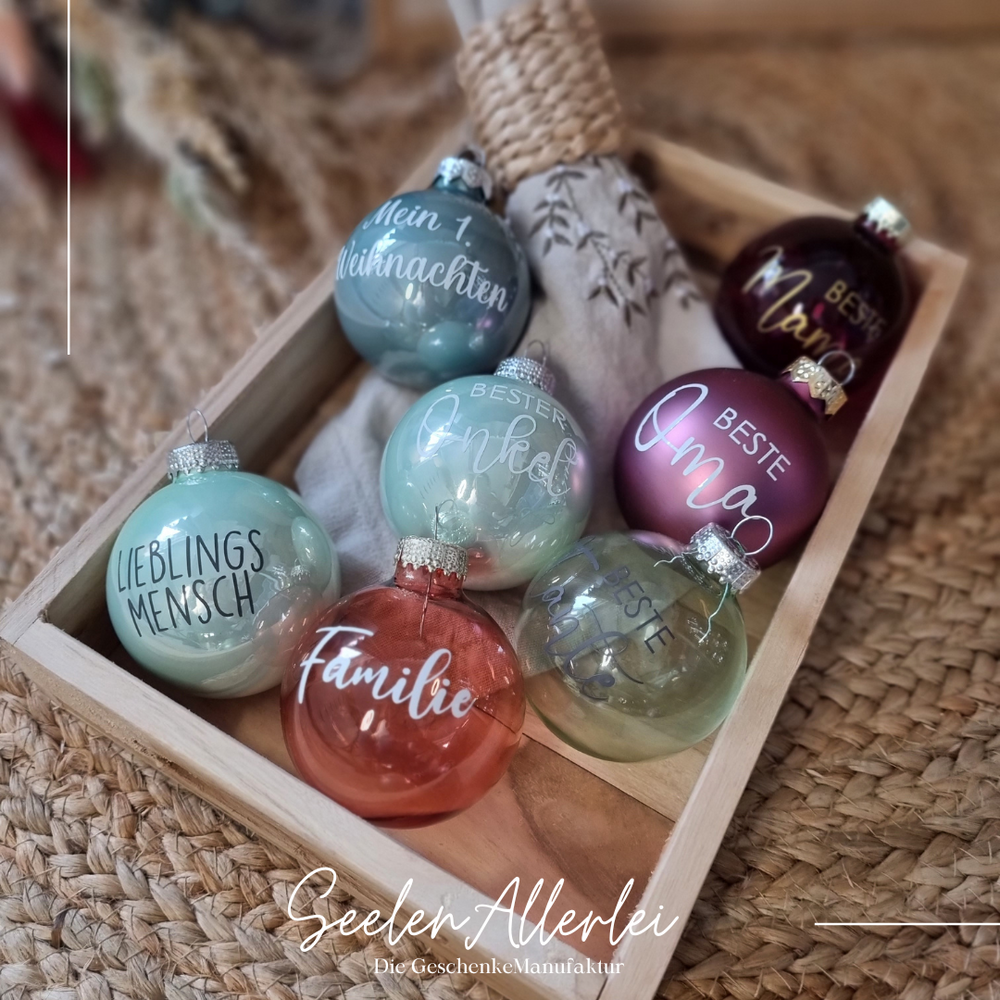 verschiedene bunte Weihnachtsbaumkugeln liegen auf einem Tablette mit verschiedene Sprüchen und Texten drauf