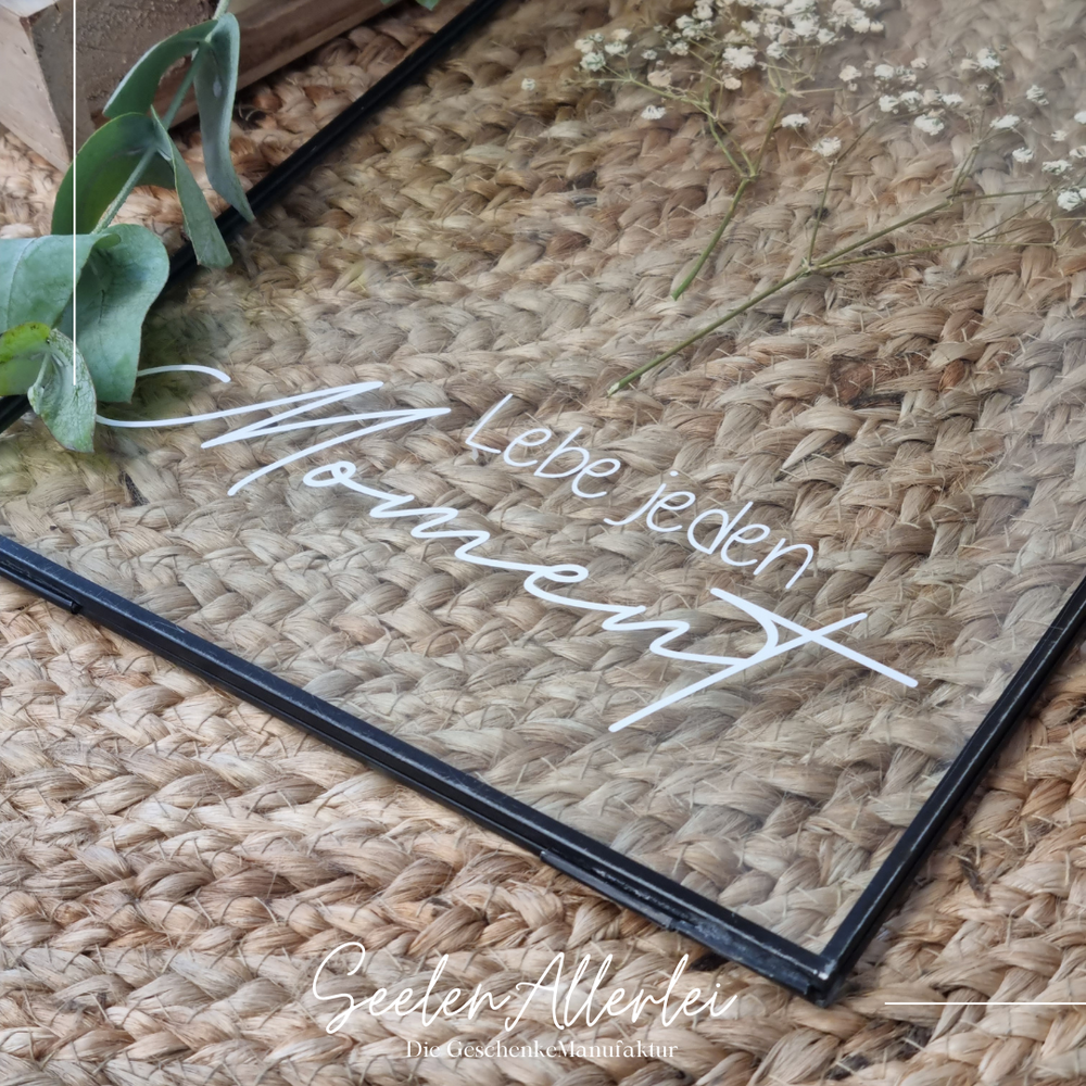 Detailaufnahme schwarzer Glasrahmen mit der Aufschrift Lebe jeden Moment