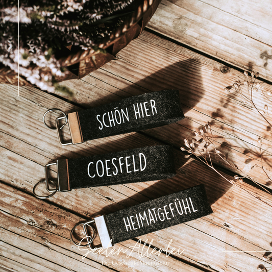 Schlüsselanhänger mit verschiedenen Aufschriften auf grauem Baumwollfilz - alle liegen auf einem Holzuntergrund