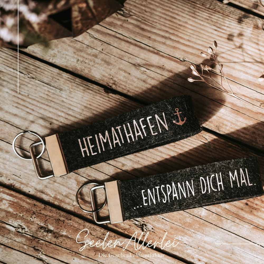 Schlüsselanhänger liegen auf einem Holzuntergrund - sie haben die Aufschrift Heimathafen und Entspann Dich mal.