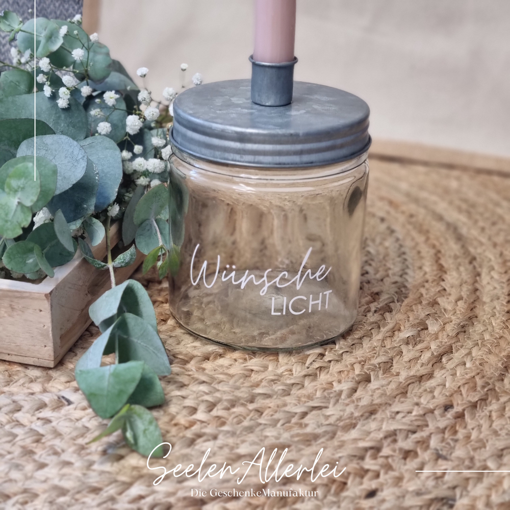 Kerzenglas mit zinkfarbenen Metalldeckel, auf dem Wünschelicht steht, steht auf dem Bambusuntersetzer mit Eukalyptusdekoration