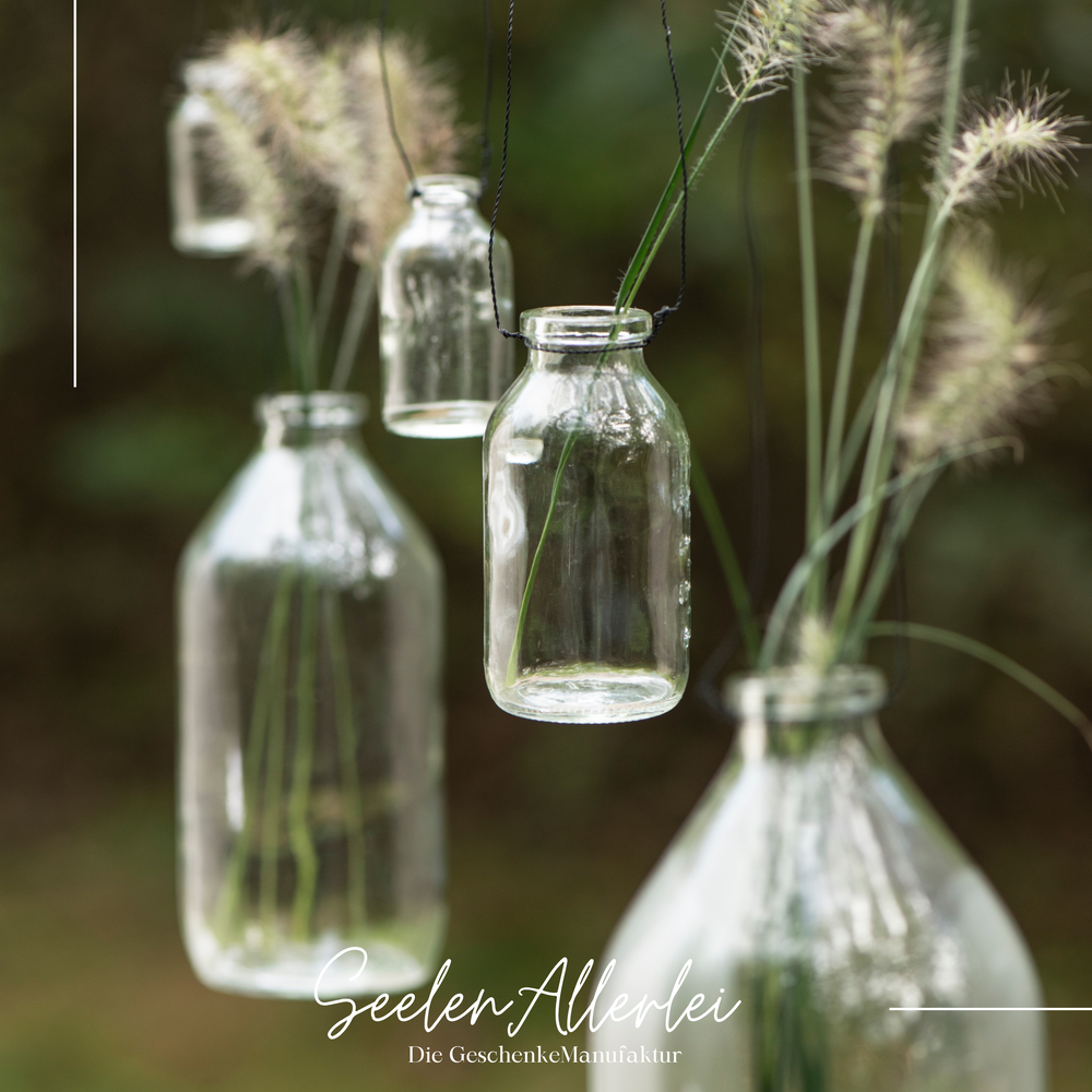viele kleine Glasflaschen hängen vor dem Fenster mit ein paar Trockenblumen