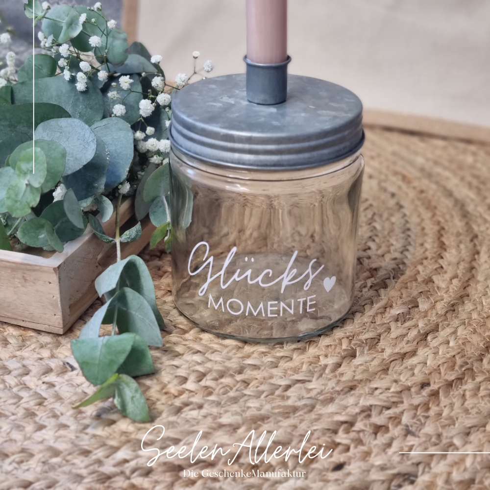 Glücksmomente steht in weißer Schrift auf einem Kerzenglas mit zinkfarbenem Deckel
