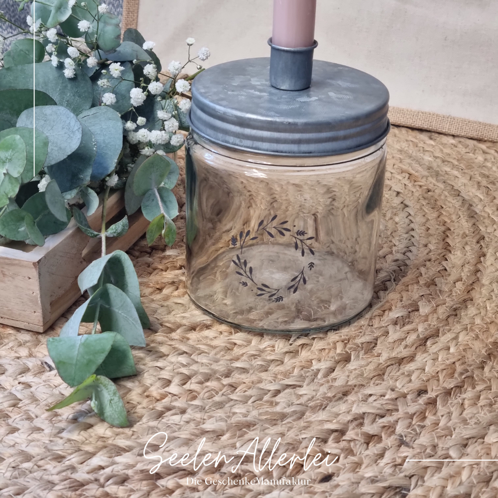 schwarzer Kranz aufgedruckt auf einem Kerzenglas mit Metalldeckel mit Eukalyptusdekoration daneben