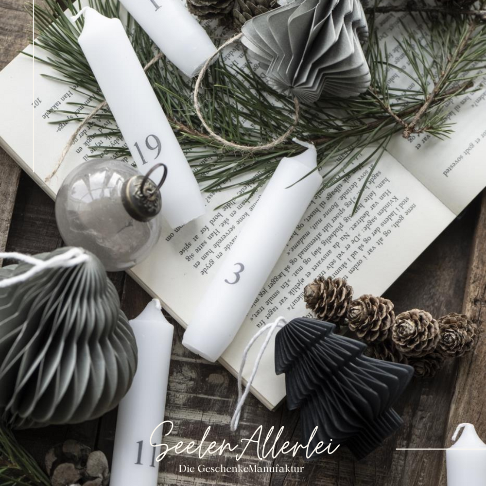 mehrere Tannenbaumanhänger aus Papier liegen mit Kerzen auf einem aufgeschlagenen Buch