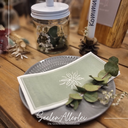 grüne Serviette liegt mit einem Eukalyptusblatt auf einem Teller von IBlaursen auf einem Holztisch mit tischdekoration