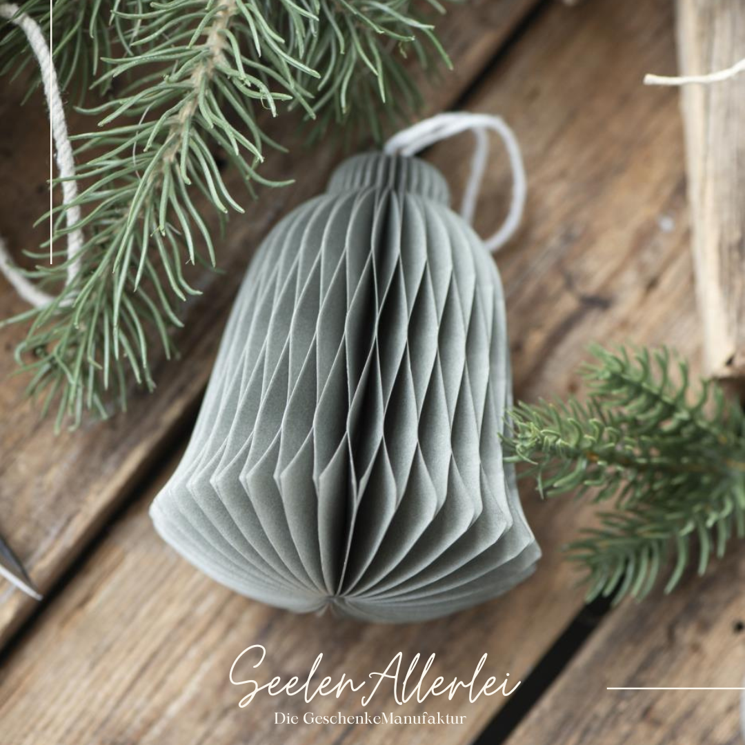 Weihnachtsbaumanhänger aus Papier mit Magnetverschluss in Form einer grauen Glocke liegt auf einem Holztischmit Tannenzweigen