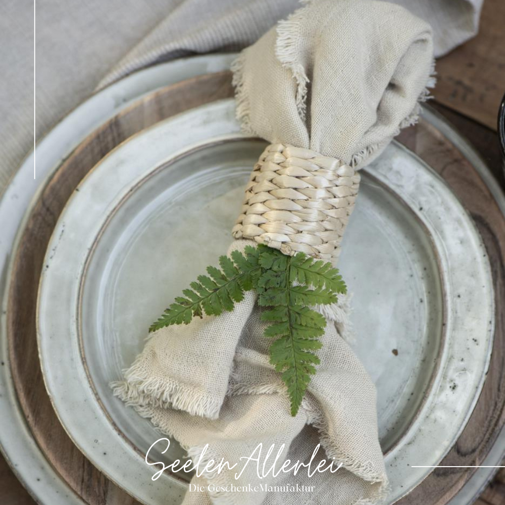 Serviettenring aus Bambus geflecht mit einer Serviette liegt auf einem schön eingedecktem Tisch mit zwei Tellern