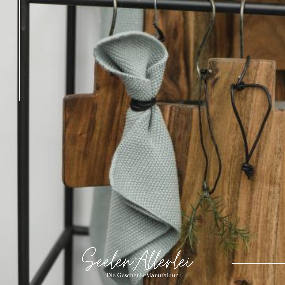 Spültuch in der Farbe beige hängt an einer Hakenleiste zusammen mit einem Holzbrett und einem Kräuterzweig